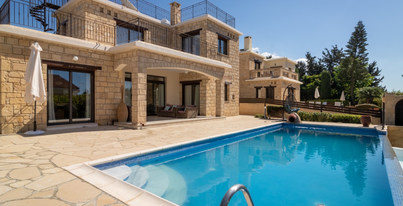 A spacious stone-built villa with traditional Mediterranean architecture features a private swimming pool, covered outdoor lounge, and multiple balconies with panoramic terraces. Blending timeless design with modern comforts, the villa offers an inviting setting for a relaxing holiday in Cyprus.