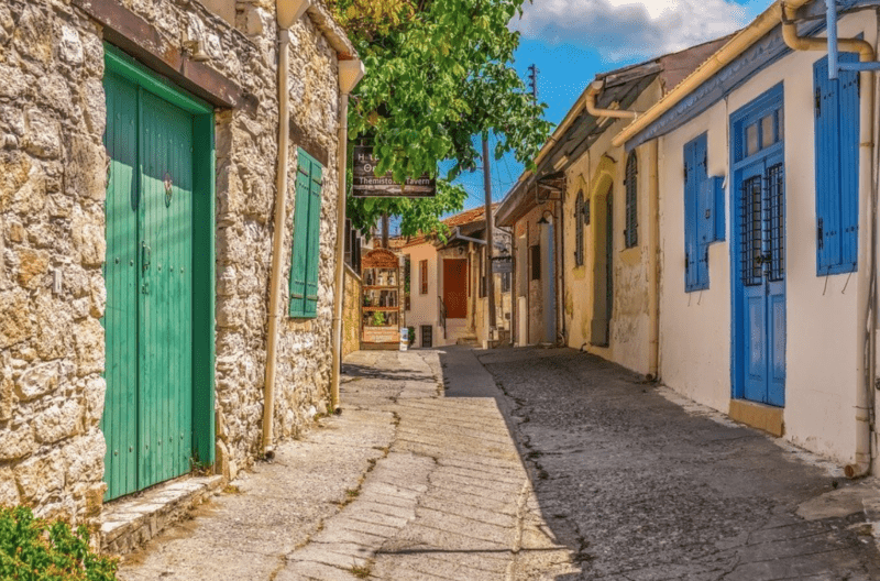 Narrow cobbled street in Omodos village lined with traditional stone houses featuring blue doors and windows in Cyprus.