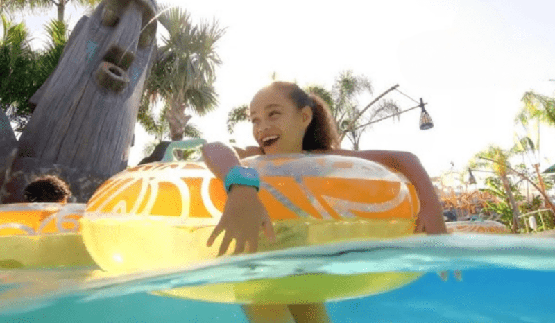 A smiling girl riding a water slide on a yellow inflatable at Paphos Aphrodite Waterpark in Cyprus.