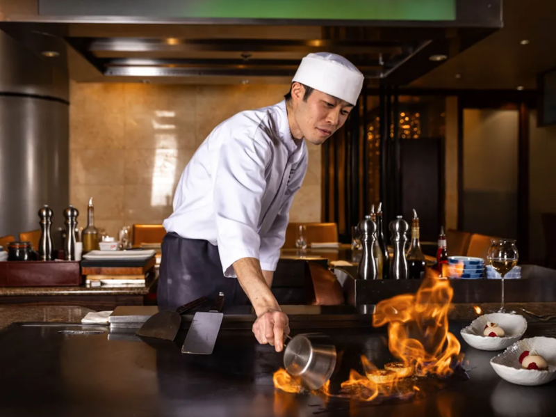 Chef in uniform cooking at a teppanyaki grill with flames at Samisen Teppanyaki restaurant in Cyprus.
