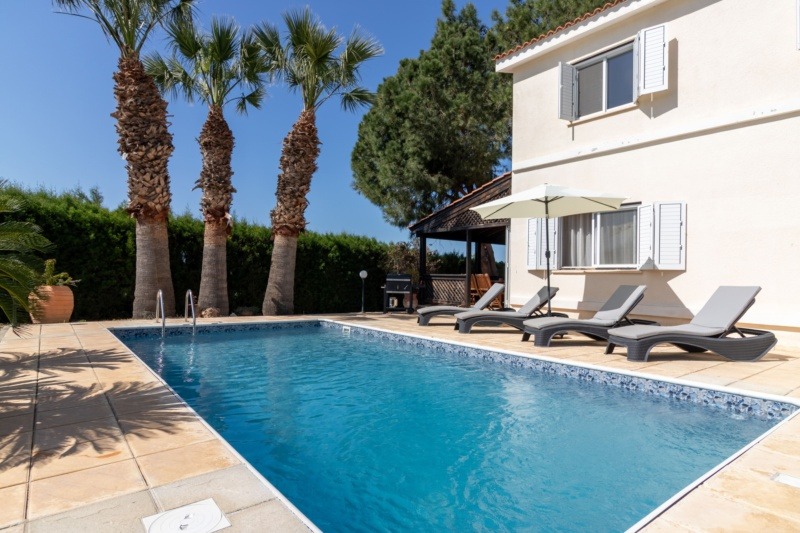 Modern villa with a swimming pool, sun loungers and palm trees under a clear blue sky in Cyprus.