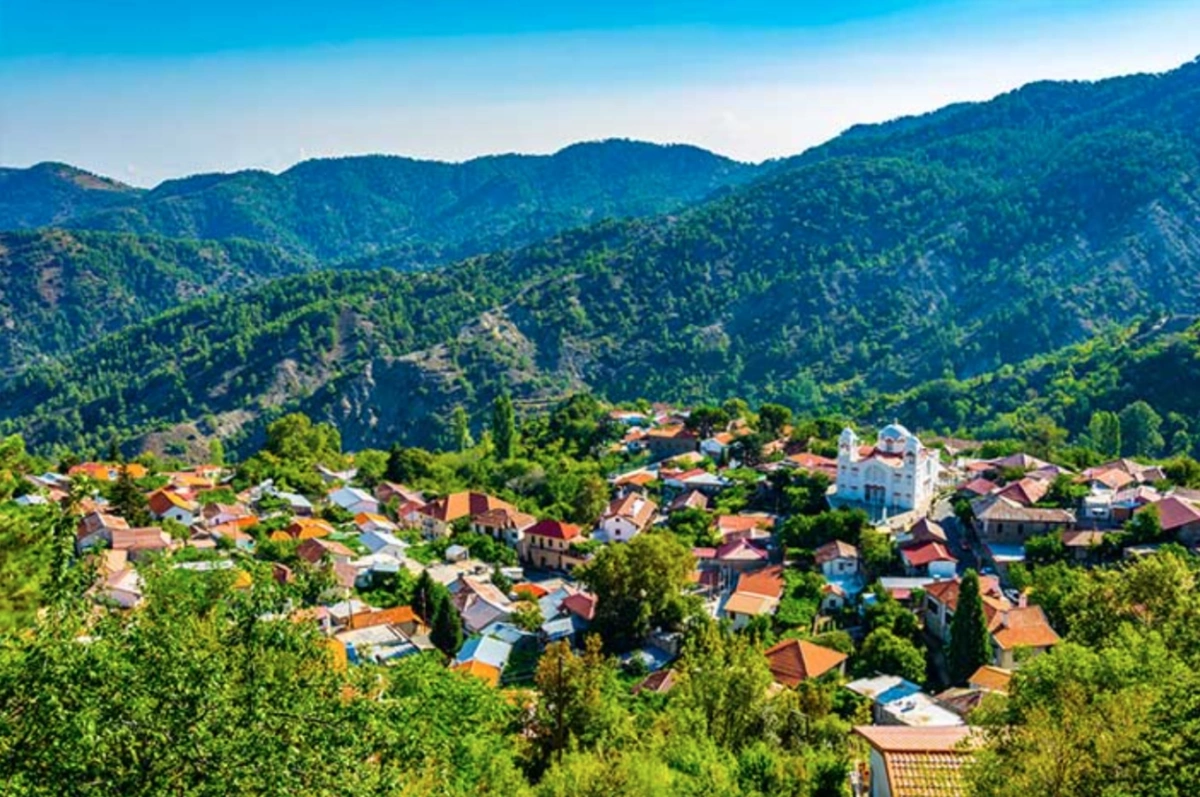 Aerial view of a traditional mountain village with red-roofed houses nestled among the green forested Troodos hills of Cyprus.