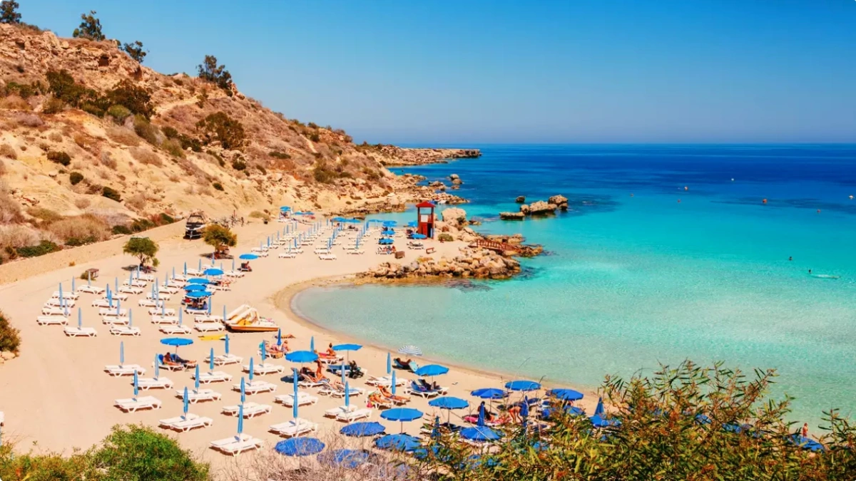 A sheltered sandy cove with sunbeds and umbrellas beside clear turquoise water at a Cyprus beach.