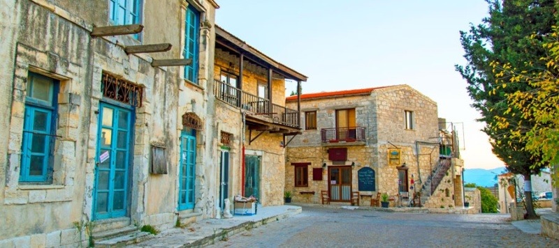 Traditional stone houses with blue-framed windows and doors along a narrow street in Kathikas village, Cyprus.