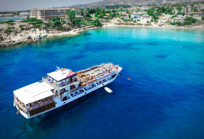 Wave Dancer cruise boat anchored in a turquoise bay along the rocky coastline near Paphos, Cyprus.