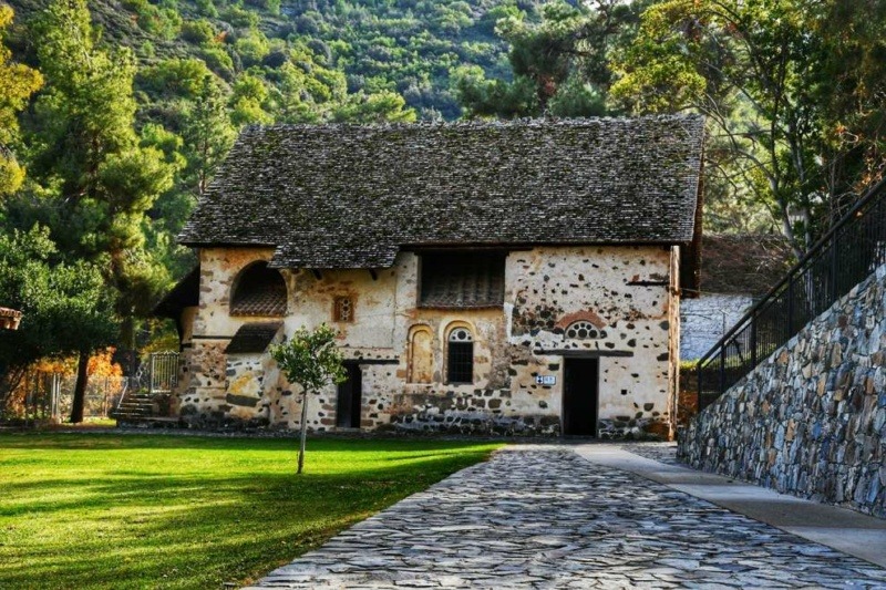 Old stone Byzantine church of Agios Nikolaos tis Stegis with a distinctive steep double timber roof, set among green trees in the Troodos Mountains of Cyprus.