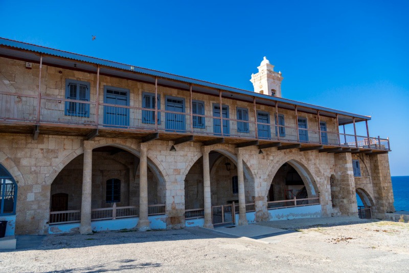 Long stone building of Apostolos Andreas Monastery with rows of arches beside the sea under a clear blue sky in the Karpas peninsula, Cyprus.