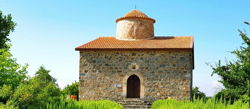Timios Stavros Church in Pelendri, a small medieval stone church with a red-tiled roof, surrounded by greenery in the Troodos region of Cyprus.